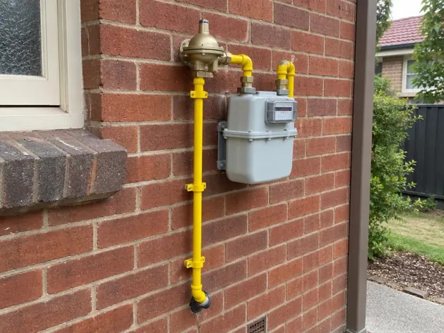 Outdoor gas meter and yellow pipework mounted on a brick house wall in Beecroft